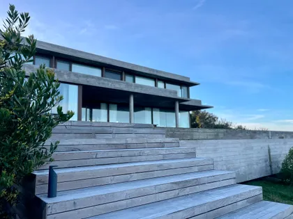 Fachada moderna con escaleras de madera y cielo azul — proyecto CASA sobre el MAR, por Guerrero Arquitectos, en Pinamar