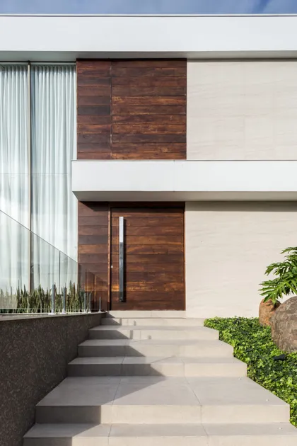 Fachada moderna con paneles de madera, piedra y ventanales con escalera de baldosas — proyecto Casa MC, por Boscardin Corsi Arquitetura