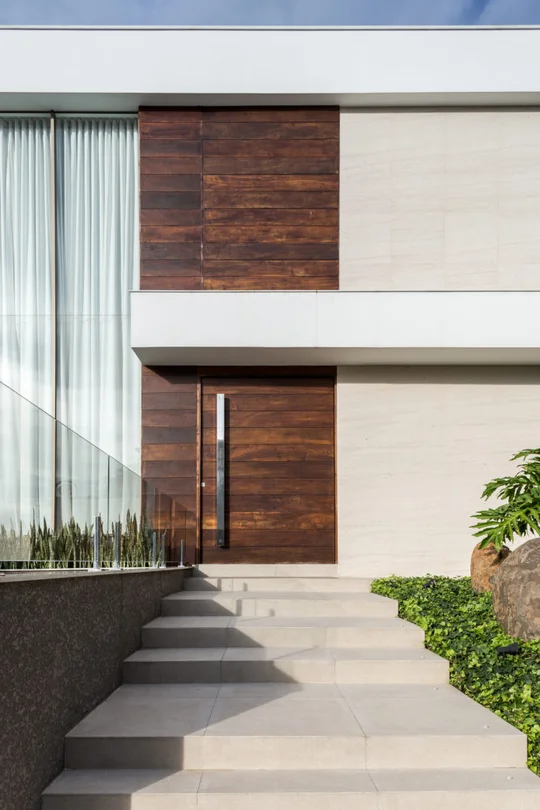 Fachada moderna con paneles de madera, piedra y ventanales con escalera de baldosas — proyecto Casa MC, por Boscardin Corsi Arquitetura