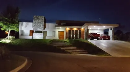 Casa moderna de noche con fachada de hormigón y madera — proyecto LA RESERVA CARDALES LRCC 121, por LESSI ARQUITECTURA, en Los Cardales