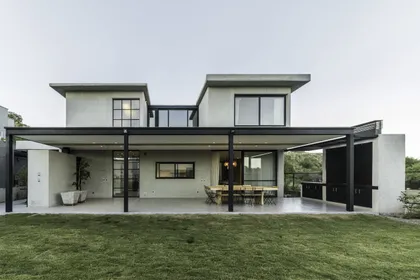 Casa moderna blanca con pérgola negra y jardín verde frontal — proyecto CASA ARFE, por Valeria Valdivieso Arquitecta, en Ciudad de Mendoza