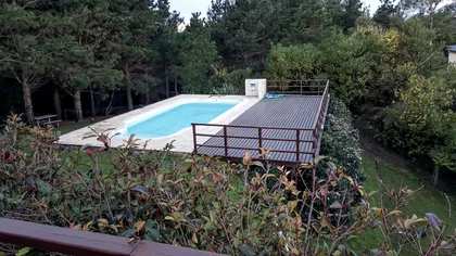 piscina moderna con deck de madera y vegetación frondosa — proyecto Vivienda Unifamiliar en Costa Esmeralda, por Estudio Schifano, en Costa Esmeralda
