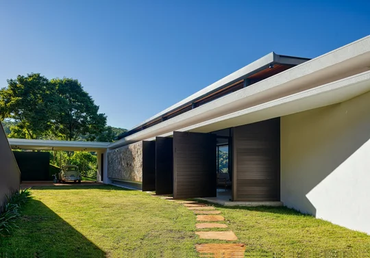 Casa moderna con fachada blanca, techos volados negros y jardín verde — proyecto Casa das Pedras, por Tetro Arquitetura