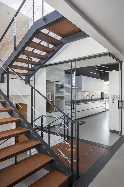 Escalera de madera con barandal negro y cocina moderna al fondo — proyecto Casa 636, por Coda Arquitetos