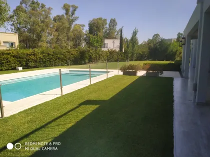 Amplia vista de piscina moderna rodeada de césped y vegetación frondosa — proyecto Vallegas, por Esudio Arq. Varise Aldo, en B1648 Tigre