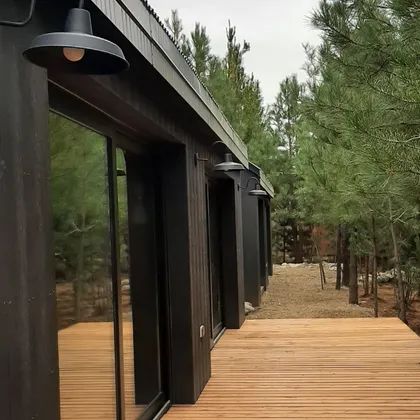 fachada moderna de madera oscura con deck y luces colgantes — proyecto Casa LA MOROCHA, por Showhouse Bariloche, en San Carlos de Bariloche