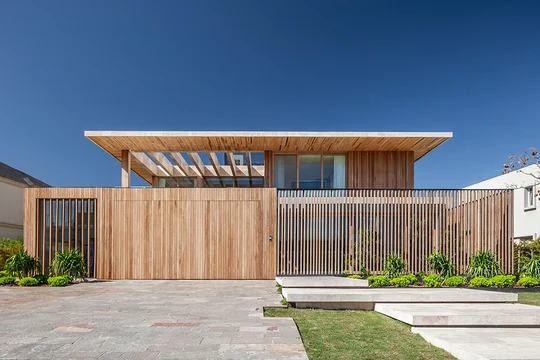 Fachada de casa moderna con revestimiento de madera y grandes ventanales — proyecto Casa JIB, por MUCHTEK, en Nordelta