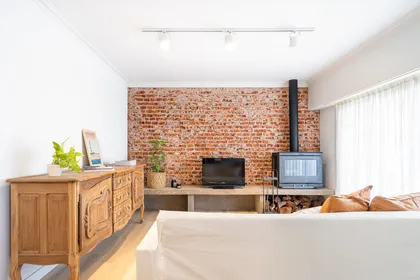 Sala de estar rústica con pared de ladrillos y estufa a leña — proyecto REFROMA GUERNICA, por Maria Menna Arquitecta, en Mar del Plata