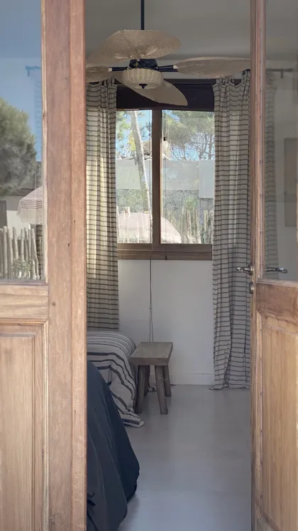 Dormitorio rústico con ventilador de techo de mimbre y cortinas a rayas — proyecto El Refugio, por Grupo Pauta Arquitectura, en Pinamar