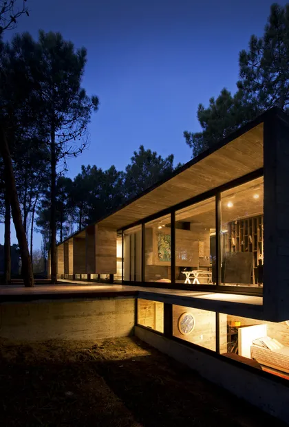Casa moderna de noche con fachada iluminada entre árboles — proyecto Casa Valeria, por Luciano Kruk