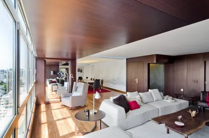 Living moderno con ventanales y paneles de madera oscura — proyecto Departamento Nuñez, por Claudia Faena Studio, en Núñez