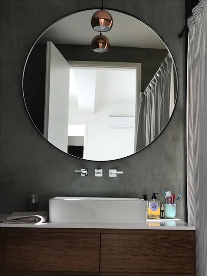 Baño moderno con espejo redondo, lavabo de cerámica y luces cobre — proyecto Casa Las Liebres, por Mazzinghi Sanchez, en Garin