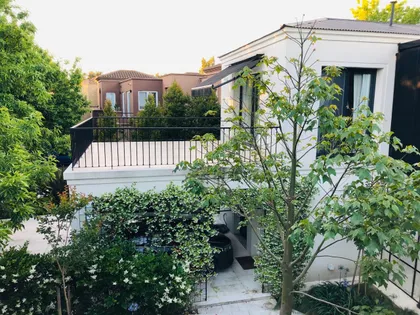 Fachada moderna con vegetación exuberante y terraza de madera — proyecto CASA DEL PUENTE, por Estudio Xime Fontan Balestra, en General Pacheco