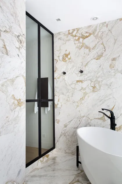 Baño moderno con mármol blanco, bañera blanca y mamparas negras — proyecto BM House, por Studio Ro-ca