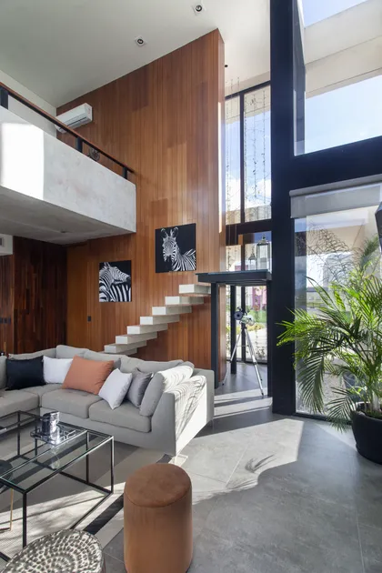 Living moderno con pared de madera, escalera flotante y sofá grande — proyecto Casa BJM, por Vanguarda Arquitectos, en Belén de Escobar