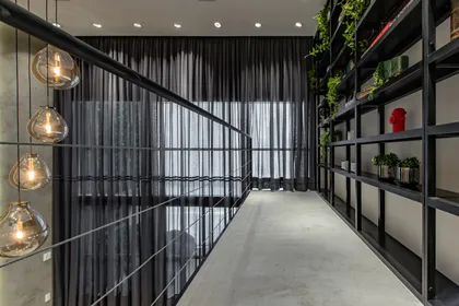 Pasillo industrial con escalera, plantas colgantes y lámparas cálidas — proyecto Duo Morumbi, por Pricila Dalzochio