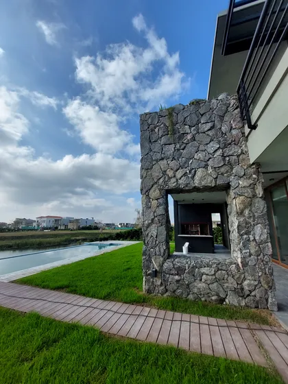 Pileta infinita y quincho moderno con estructura de piedra y deck — proyecto Puertos del Lago - Muelles, por CM Espacio & Arquitectura, en Belén de Escobar