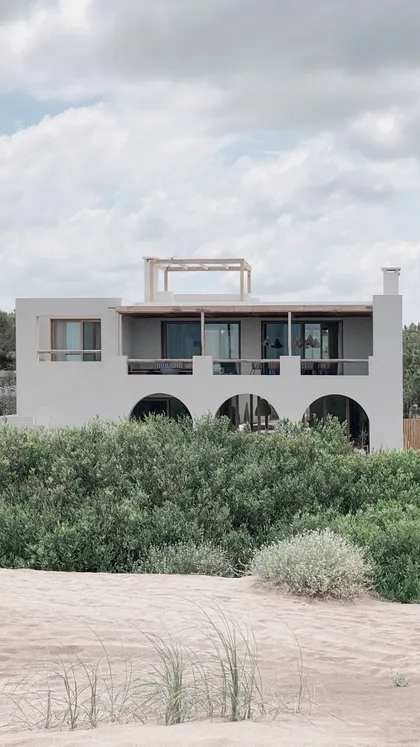 Casa blanca moderna mediterránea con arcos y vegetación costera — proyecto El Refugio, por Grupo Pauta Arquitectura, en Pinamar