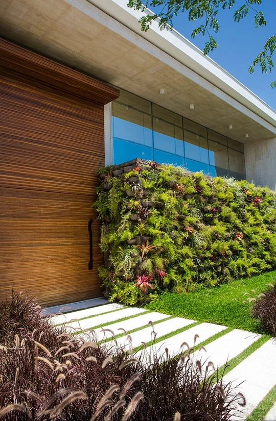 Fachada contemporánea con jardín vertical y puerta de madera — proyecto Arquitetura e Interiores II, por Demian Golovaty