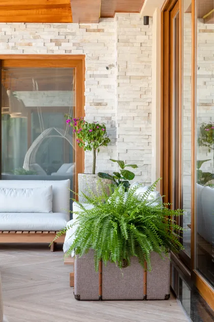 Terraza moderna con fachada de piedra, sofá y plantas en macetas — proyecto Projeto Destaque Club&Casa, por OKA ARQUITETURA
