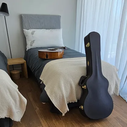 dormitorio moderno con cama beige y funda de guitarra negra — proyecto Estancias , por Claraboia , en Pilar