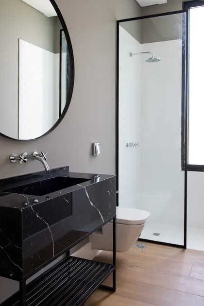 Moderno baño con vanitory de mármol negro y espejo redondo — proyecto Bosque Chico, por Estudio Arq. María Sioli, en Garin