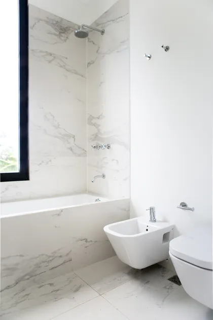 Baño moderno con revestimiento de mármol blanco, bañera, bidet y ducha — proyecto Bosque Chico, por Estudio Arq. María Sioli, en Garin