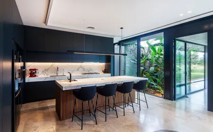 Cocina moderna con isla grande, ventanas de piso a techo y vegetación exuberante — proyecto BUNKER, por OON ARCHITECTURE