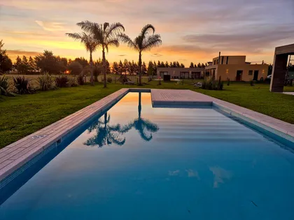 Pileta infinita al atardecer con palmeras y casa moderna de fondo — proyecto Casa Golf, por RY Construir Estudio, en San Vicente