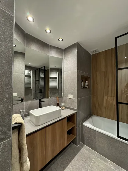 Baño moderno con revestimientos de piedra gris y mueble de madera — proyecto Salguero II, por MDBK Arquitectura, en Palermo