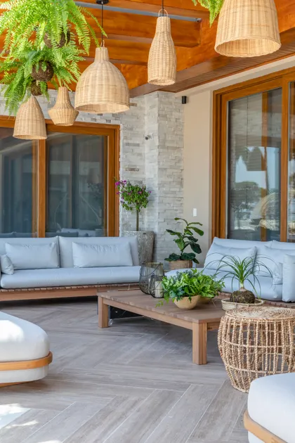 Terraza exterior con sillón de madera, mesa ratona y luces colgantes de ratán — proyecto Projeto Destaque Club&Casa, por OKA ARQUITETURA