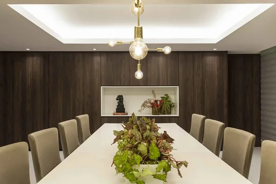 Comedor contemporáneo con mesa blanca, sillas beige y pared madera oscura — proyecto Jantar, por Xico Diniz