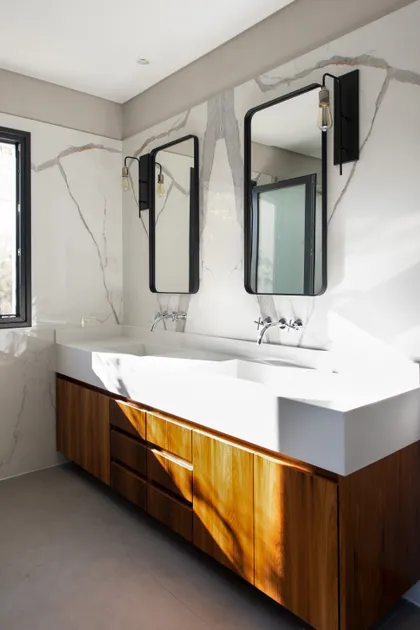 Baño moderno con lavabos dobles integrados, mueble flotante de madera y paredes de mármol — proyecto EL ENCUENTRO , por Greschek Obras , en Benavidez