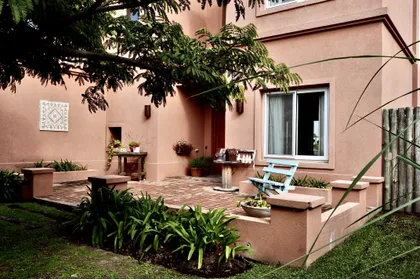 Fachada terracota con patio adoquinado y frondosa vegetación exterior — proyecto Santa Teresa, Villanueva, por Marconi Silva Arquitectos, en Benavidez