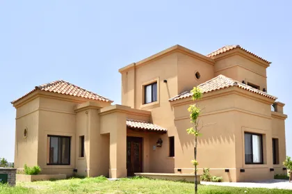 Casa residencial color beige con techos de tejas y jardín exterior — proyecto San Marcos, por Marconi Silva Arquitectos, en Benavidez