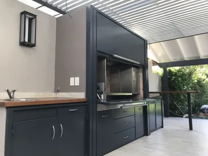 Quincho moderno con isla de acero inoxidable y detalles en madera — proyecto Casa Beccar, por Rioja Arquitectura, en Béccar