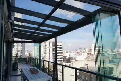 terraza moderna con puertas de vidrio plegables y vista urbana — proyecto TOLDER - TECHOS DE VIDRIO, por Argentina en Obra 2024, en Rincón de Milberg