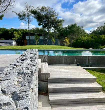 Pileta infinita con deck de madera y muro de piedra — proyecto CASA sobre el MAR, por Guerrero Arquitectos, en Pinamar