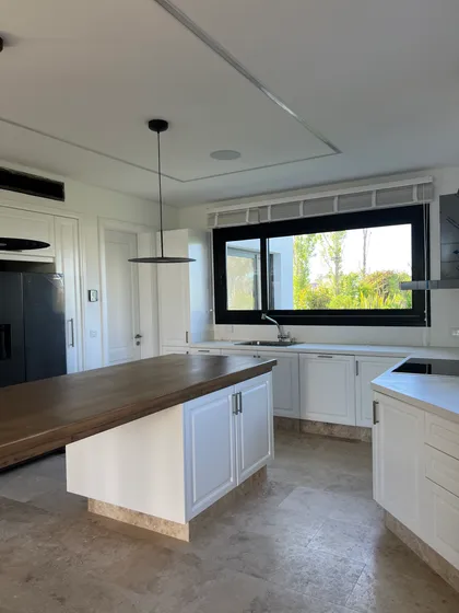 Cocina moderna con isla de madera, muebles blancos y amplios ventanales — proyecto CASA LR 456 - SOFITEL LOS CARDALES, por Carolina Depetris, en B2814 Los Cardales