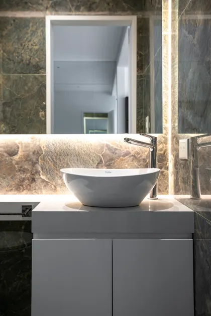 baño moderno con revestimiento de piedra y bacha de apoyo — proyecto Obra Martinez A, por Arq. Lourdes Yarade Saravia, en Martínez