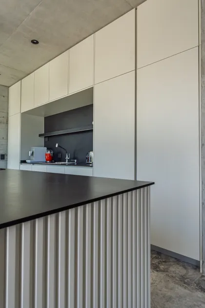 Cocina moderna con muebles blancos, encimera negra y detalles de hormigón — proyecto La Martona - Estudio Barcelona, por ABEJA CONCEPT, en Cañuelas