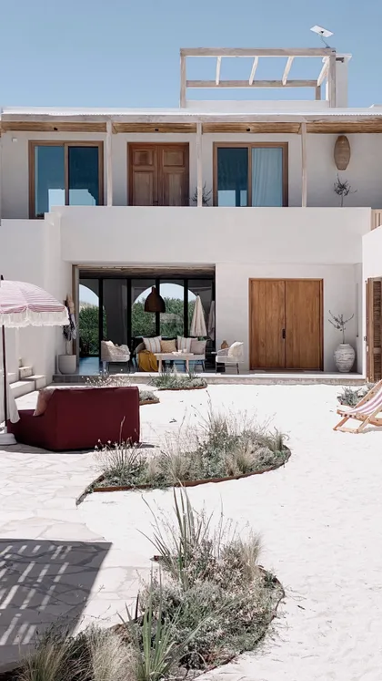 Fachada blanca mediterránea con sofá rojo y vegetación seca — proyecto El Refugio, por Grupo Pauta Arquitectura, en Pinamar