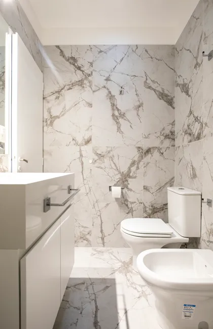 Baño moderno con mármol veteado, vanitory blanco y bidet — proyecto Obra Martinez A, por Arq. Lourdes Yarade Saravia, en Martínez