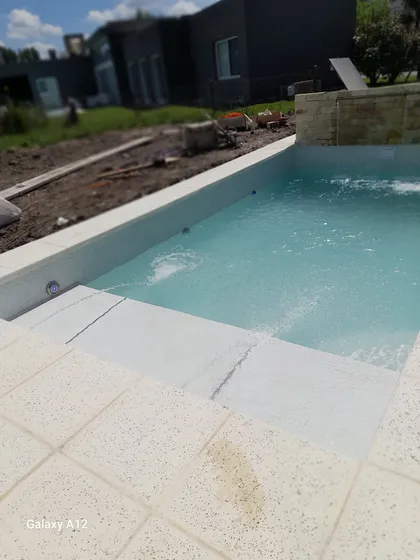 Pileta turquesa con deck de piedra y obra en fondo — proyecto piscina con playa humeda mas cascada, por Piscinas omar, en Canning