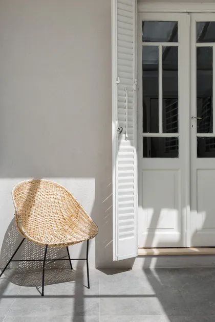 Silla de mimbre junto a puertas blancas y persianas — proyecto CARACAS, por La Nave Arq., en Villa Devoto