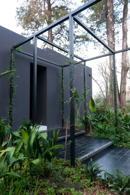 Fachada moderna brutalista con pérgola de metal y vegetación exuberante — proyecto Casa M, por Estudio Dado, en Pilar