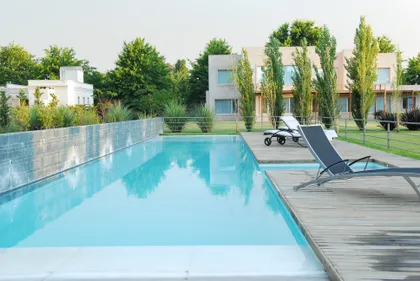 Piscina moderna rodeada de deck de madera y vegetación frondosa — proyecto Pilar House , por Vanguarda Arquitectos, en Pilar