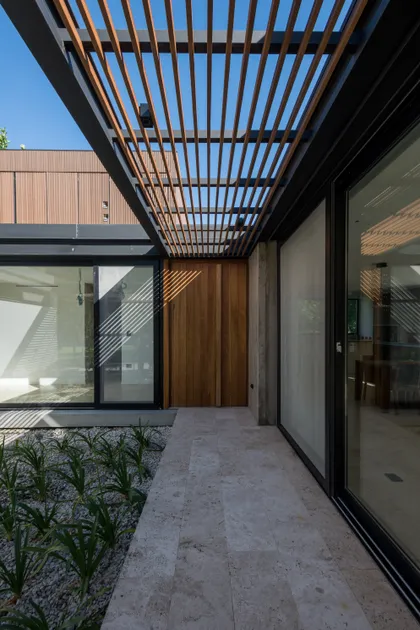 Fachada moderna con pérgola de madera y piedra — proyecto CASA AC , por BUSCETTI & DI BERNARDO arquitectas, en Villa Elisa