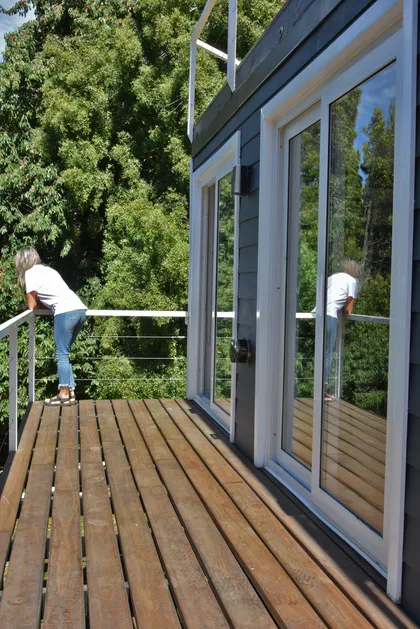 Mujer en balcón de madera con vista a bosque y ventanas amplias — proyecto Departamento CV, por Quetuna Interiores, en San Carlos de Bariloche