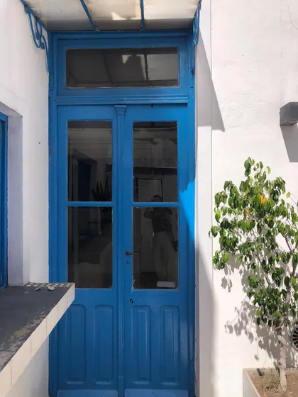 Fachada mediterránea con puerta azul y toldo — proyecto Abel & Gaby, por Costantini studio, en Buenos Aires